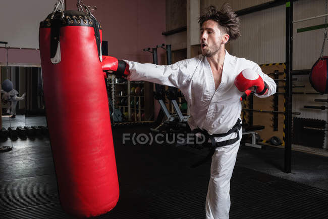 Uomo che pratica karate con sacco da boxe in palestra — Foto stock