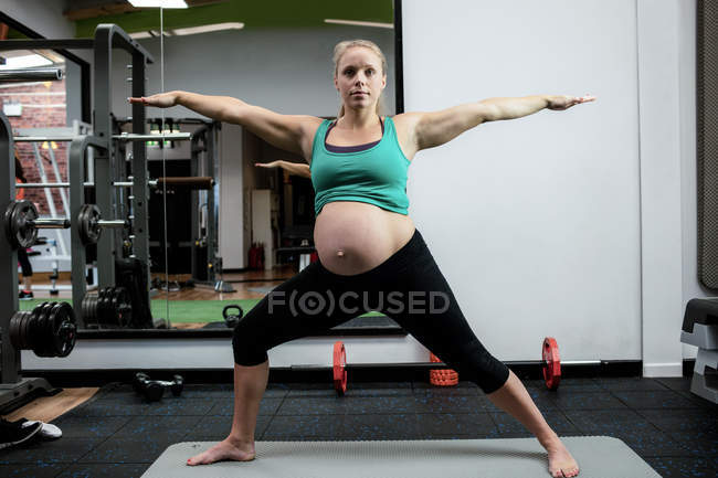 Mujer embarazada realizando ejercicio de estiramiento en la esterilla de ejercicio en el gimnasio - foto de stock