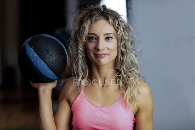 Retrato de una hermosa mujer sosteniendo una pelota de ejercicio en el gimnasio - foto de stock