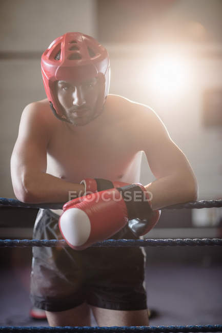 Boxer masculino em protetor boxe capacete inclinado em cordas de anel de boxe no estúdio de fitness — Fotografia de Stock