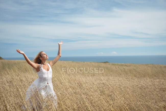 Беззаботная блондинка, стоящая в поле с поднятыми руками — стоковое фото