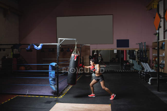 Female boxer practicing boxing with punching bag in fitness studio — Stock Photo