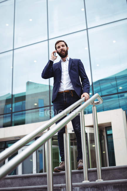 Businessman talking on mobile phone at the entrance of office building — Stock Photo