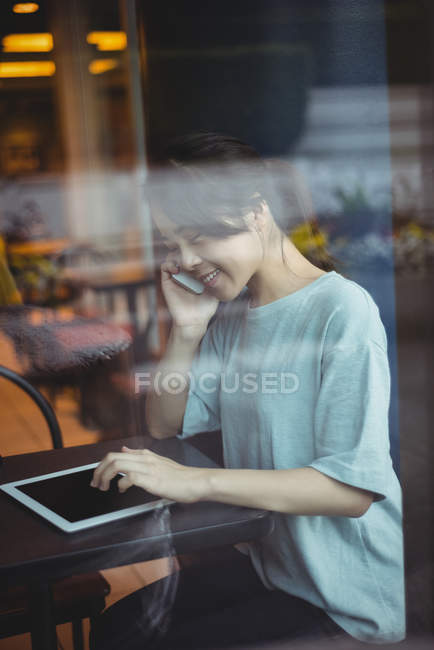 Young woman talking on mobile phone while using digital tablet — Stock Photo