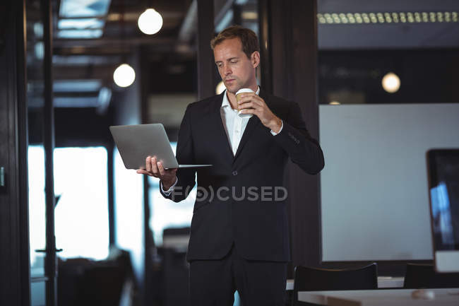 Negócios tomando café ao usar laptop no escritório — Fotografia de Stock