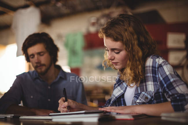 Beautiful mechanic writing in diary in workshop — Stock Photo