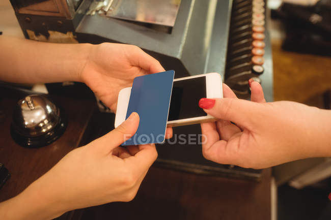 Cliente dando teléfono y tarjeta de crédito al cajero en el mostrador de facturación - foto de stock