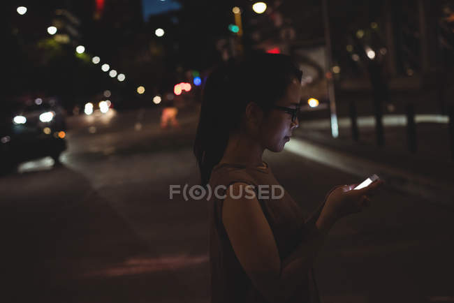 Young woman using mobile phone on street at night — Stock Photo