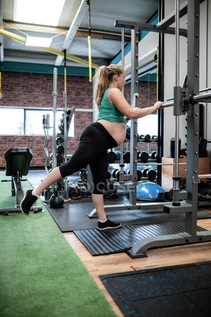 Pregnant woman exercising with fitness bar in gym — Stock Photo