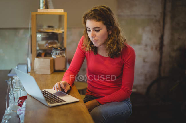 Woman sitting at counter and using laptop in bicycle shop — Stock Photo