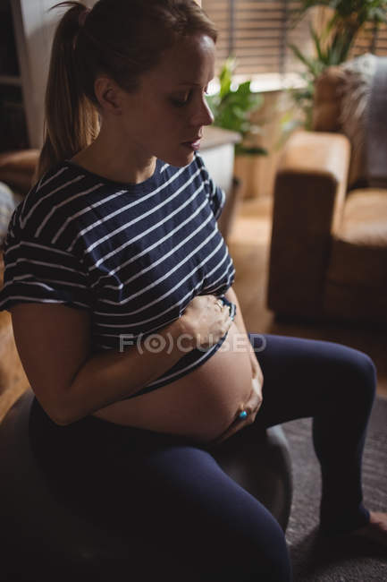 Беременная женщина сидит на тренировочном мяче в гостиной дома — стоковое фото