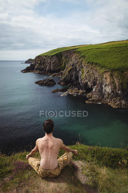 Rear view of man performing yoga on cliff — Stock Photo
