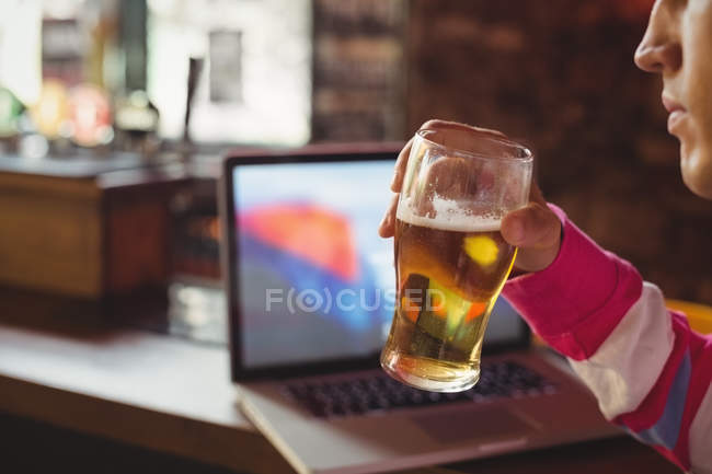 Hombre sosteniendo un vaso de cerveza en el mostrador del bar - foto de stock