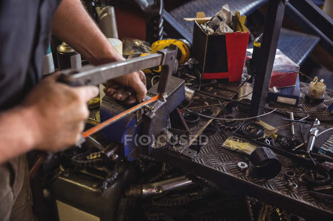 Mechanic cutting metal with hacksaw in workshop — Stock Photo