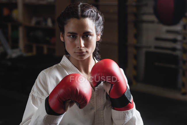 Портрет женщины-боксера в красных боксёрских перчатках, смотрящей в камеру в фитнес-студии — стоковое фото