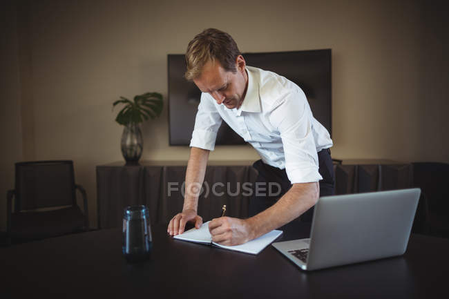 Бизнесмен пишет в блокноте на столе в офисе — стоковое фото
