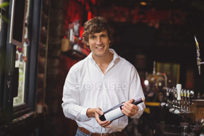 Portrait of bar tender holding a bottle of wine at bar — Stock Photo