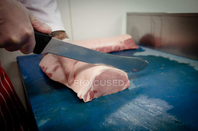 Manos de carnicero rebanando carne en la carnicería - foto de stock