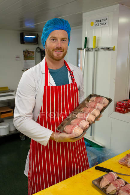 Carnicero sosteniendo una bandeja de pollo y filetes en la carnicería - foto de stock