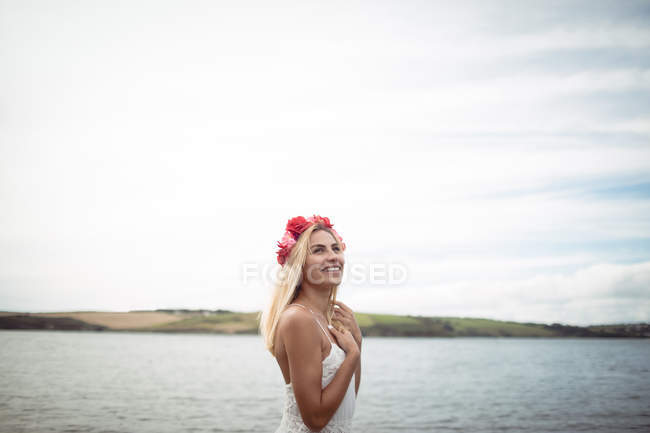 Souriant femme blonde en fleur tiare debout près de la rivière — Photo de stock