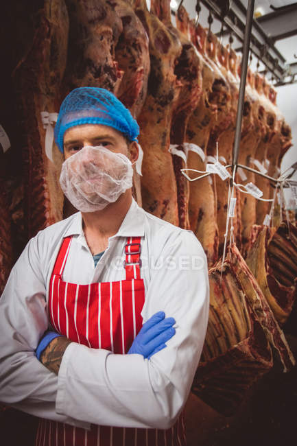 Porträt eines Metzgers, der mit verschränkten Armen in einem Fleischlagerraum der Metzgerei steht — Stockfoto