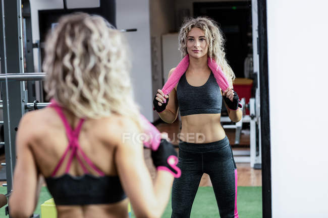 Beautiful woman standing with a towel around her neck in gym — Stock Photo