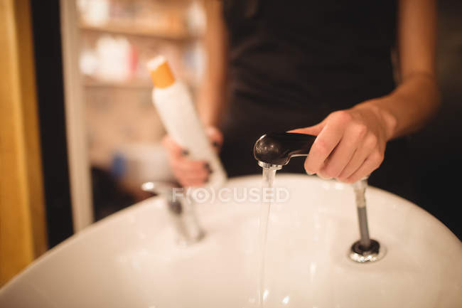 Mittelteil einer Friseurin, die im Salon einen Wasserhahn hält — Stockfoto