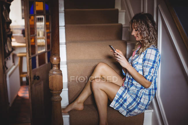 Schöne Frau, die auf der Treppe sitzt und zu Hause das Handy benutzt — Stockfoto