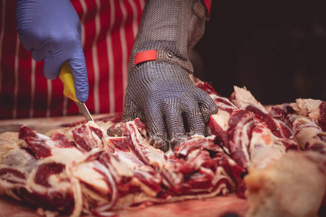 Manos de carnicero cortando carne roja en la carnicería - foto de stock
