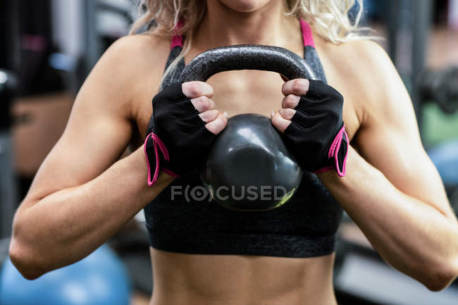 Mid-section of woman lifting kettlebell at gym — Stock Photo