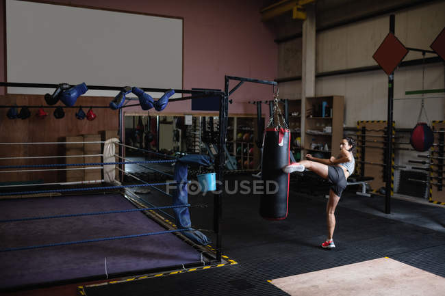 Female boxer practicing boxing with punching bag in fitness studio — Stock Photo