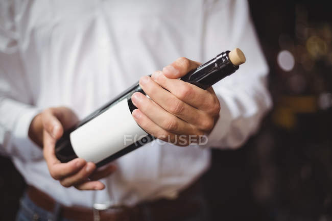 Parte média do concurso de bar segurando uma garrafa de vinho no bar — Fotografia de Stock