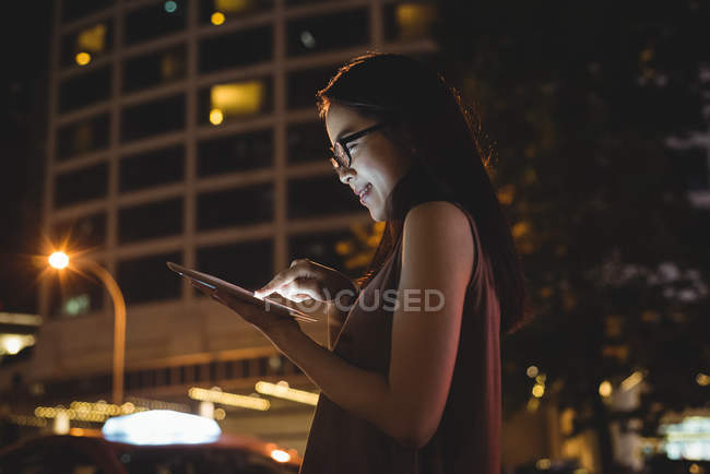 Молодая женщина использует цифровой планшет на улице ночью — стоковое фото