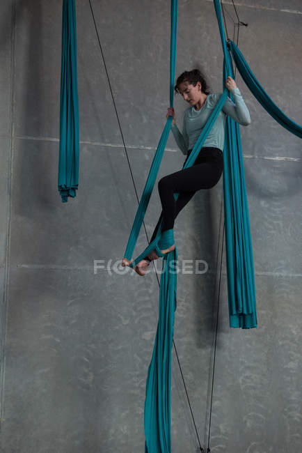 Female gymnast exercising on blue fabric rope in fitness studio — Stock Photo