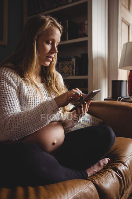 Беременная женщина использует смартфон в гостиной дома — стоковое фото