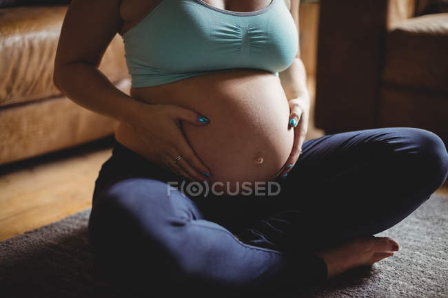 Обрезанный образ беременной женщины расслабляющий и трогательный живот в гостиной — стоковое фото