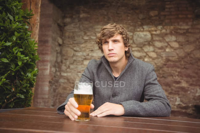Удумливий чоловік сидить у барі зі склянкою пива на столі — стокове фото