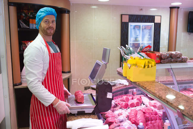 Retrato del carnicero comprobando el peso de la carne en el mostrador en la carnicería - foto de stock