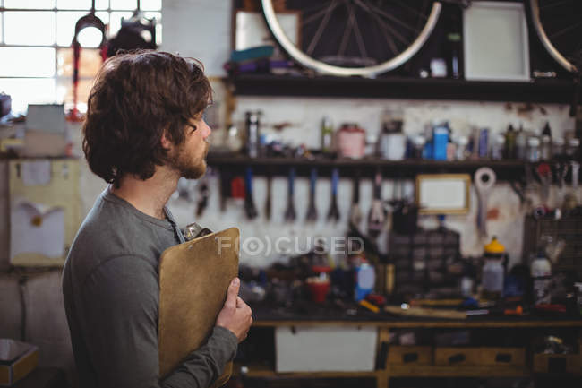 Mécanicien debout avec presse-papiers dans un magasin de vélos — Photo de stock