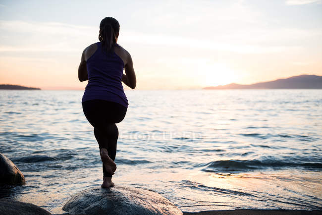 Rear view of woman practicing yoga on rock during sunset — Stock Photo