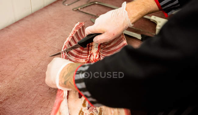 Средняя часть мясника режет рёбра туши свинины в мясной лавке — стоковое фото