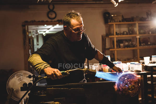 Glassblower blowing propane gas flame on finished piece of glass at glassblowing factory — Stock Photo