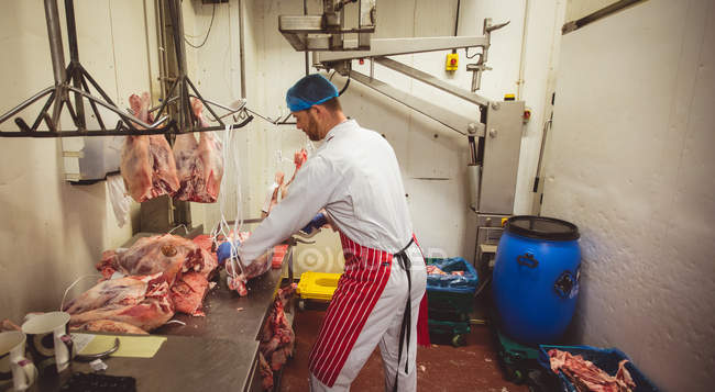 Butcher hanging red meat in storage room at butchers shop — Stock Photo