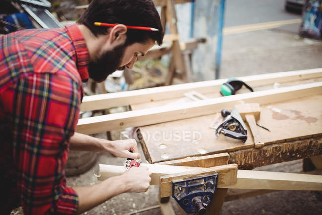 Man using a handheld tool to smooth and level the surface of a plank in boatyard — Stock Photo