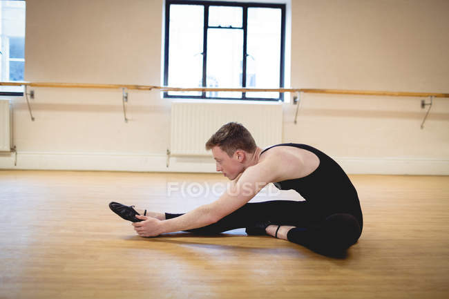 Vista lateral de bailarino realizando exercício de alongamento no chão em estúdio — Fotografia de Stock