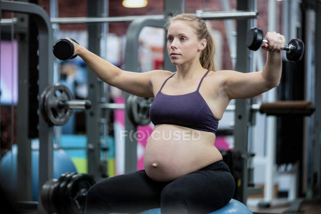 Pregnant woman lifting dumbbells at gym — Stock Photo