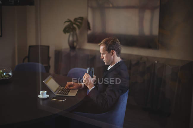 Uomo d'affari che utilizza il computer portatile mentre beve acqua in ufficio — Foto stock