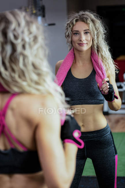 Beautiful woman standing with a towel around her neck in gym — Stock Photo