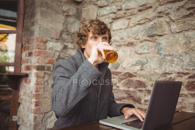 Uomo che beve birra mentre usa il computer portatile al bar — Foto stock