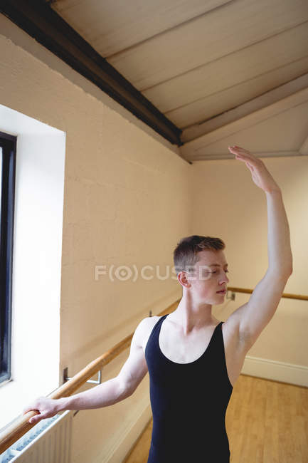 Portrait de Ballerino s'étirant sur la barre tout en pratiquant la danse de ballet en studio — Photo de stock